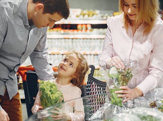 A family enjoys shopping for fresh produce together in a supermarket, smiling and bonding.