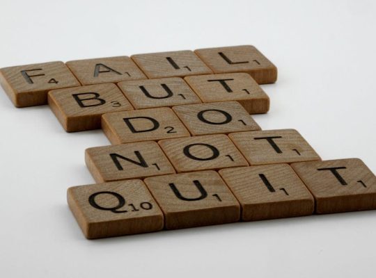 Wooden Scrabble tiles arranged to spell 'Fail but do not quit,' inspiring determination.
