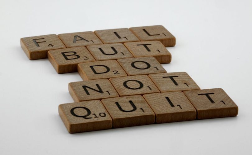 Wooden Scrabble tiles arranged to spell 'Fail but do not quit,' inspiring determination.