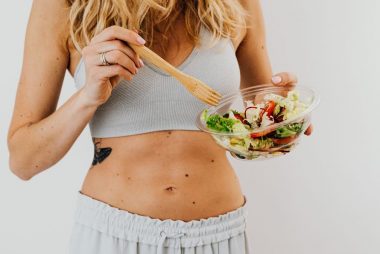 Young woman in sports attire holding a fresh salad bowl, promoting a healthy lifestyle.